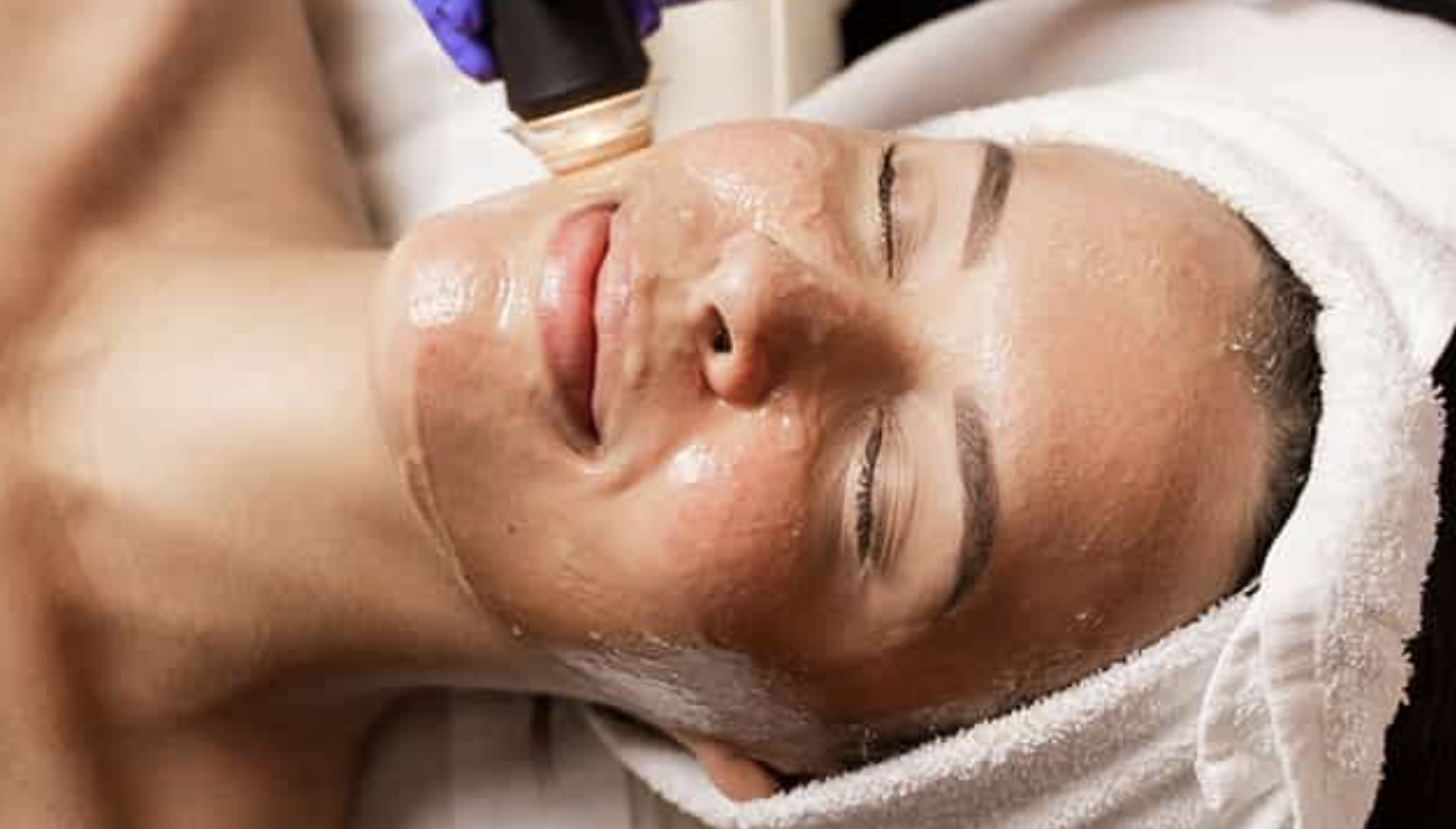 woman smiling during an Oxypod facial treatment with glowing skin and a towel wrapped around her head