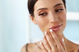 Close-up of a woman with smooth plump lips gently touching her face reflecting natural results after dermal filler treatment