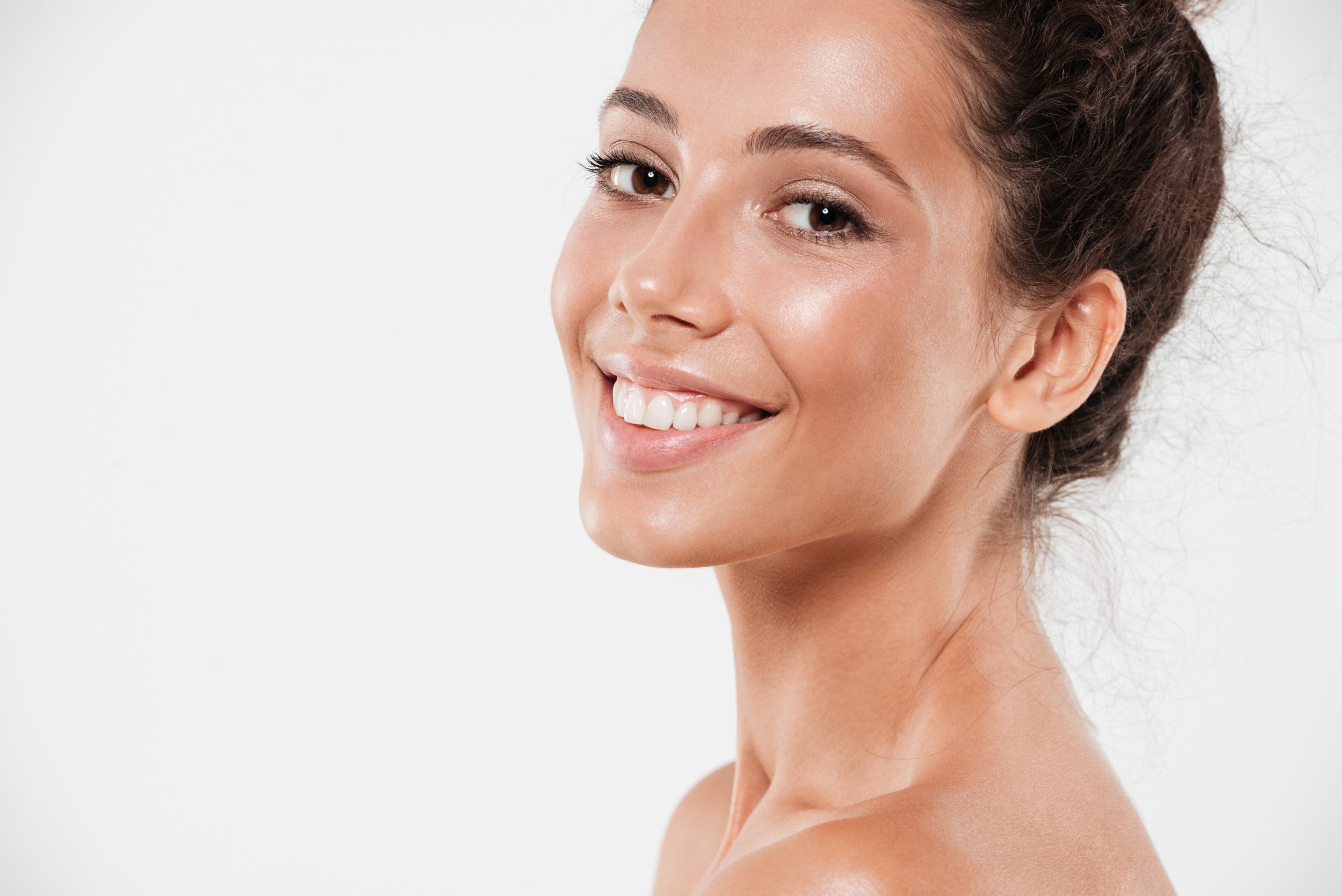 Smiling woman with radiant clear skin looking over shoulder on white background