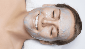Smiling woman receiving an OxyGeneo facial treatment with blue oxygenating gel applied to her face