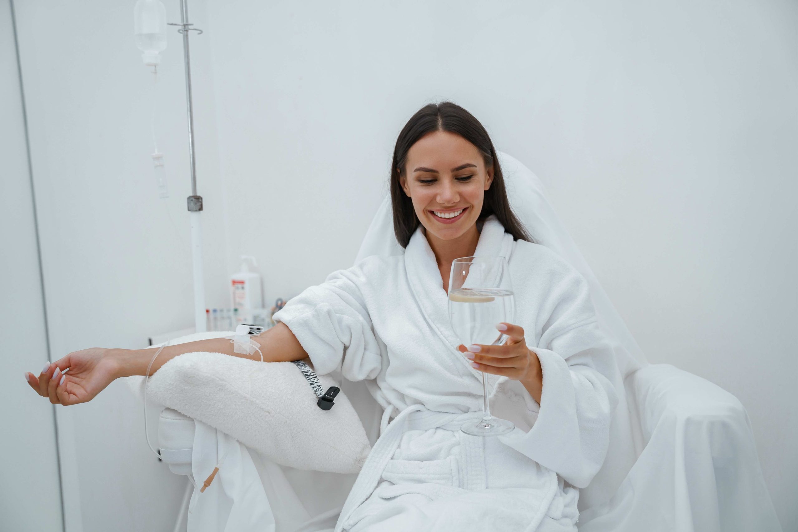 Beautiful woman in white bathrobe drink water during medical procedure in beauty clinic